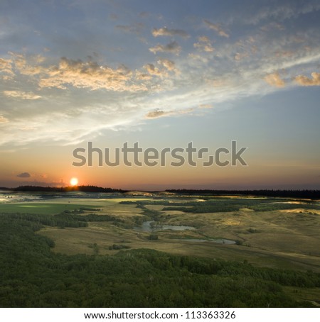 View from the top of the mountain. Colorful sunset. Blue sky and white clouds. Green field and summer forest. Beauty landscape