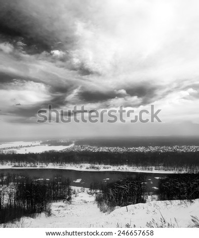 Winter landscape. Gray snowy forest and blue sky with white clouds. Cold river. Black and white photo