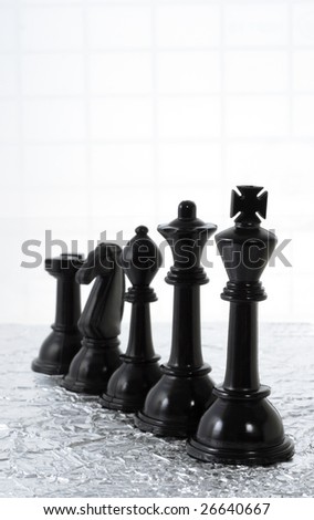 Row of black chess pieces on creased silver metallic sheet and grid background