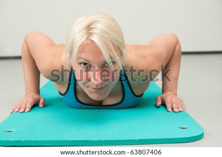 Blonde woman with focused look and ready to do push-ups on the mattress at the gym.