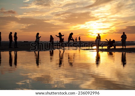 Sunset on a beach in Spain. Sand beach. Summer in Spain. People visible in a background. Posing to photos, jumping and make fun.  Landscape, romantic view