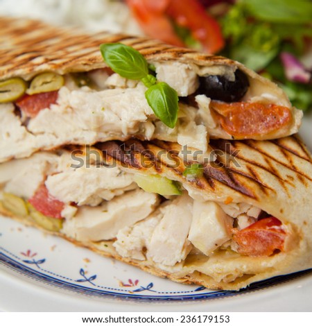 Wrap with chicken, green and black olives and dry tomatoes. Presented on white plate with blue decorations. Put with green salad and tomatoes.