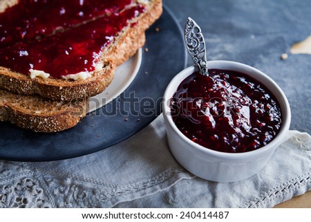 Raspberry jam - homemade jam with fresh fruits from garden. All in rustic decoration, silver spoon, Fruit jam on toasted bread and black coffee in background. Perfect for light sweet  breakfast.