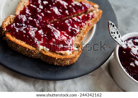 Toast with raspberry jam - homemade marmalade with fresh fruits from garden. All in rustic decoration, silver spoon, Fruit jam on toasted bread. Perfect for light sweet  breakfast.