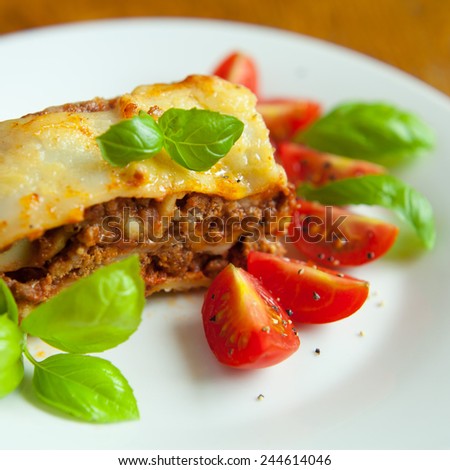 Italian lasagna with tomatoes and basil leaves presented on the white plate. Lasagna prepared with tomato sauce and beef meet with herbs and italian pasta