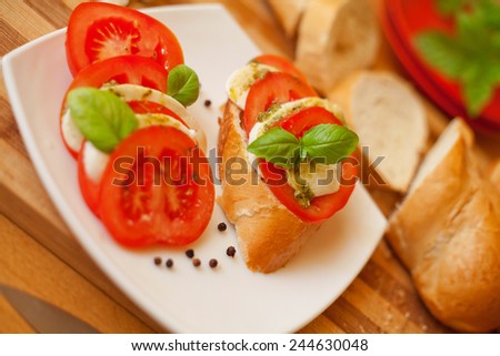 Cut mozzarella cheese and cut fresh tomatos presented on a white plate with tomato and mozzarella sandwich.Surrounded by fresh baguette.