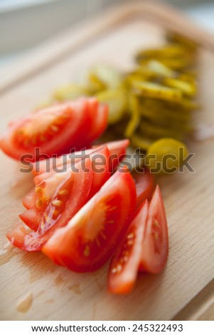 Tomato and pickled cucumber cut into pieces presented on a wooden desk. Healthy food. Preparation for breakfast. MAcro perspective. Nobody. Food and meal at home.