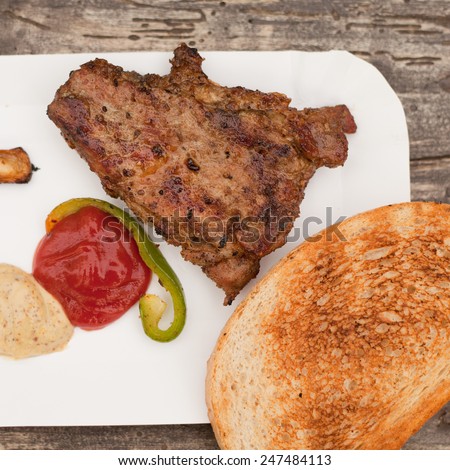 Grilled chuck steak on a white plate with grilled roll and sauces. Barbecue in a garden. pork, beef meat. Grilled meat. Food, restaurant, menu. Nobody, macro perspective.