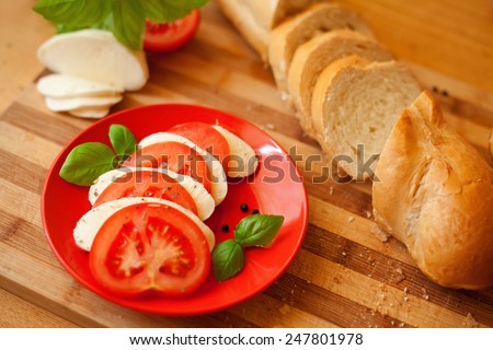 Caprese salad. Cut mozzarella cheese and cut fresh tomatoes presented on a red plate with tomato and mozzarella sandwich.Surrounded by fresh baguette.