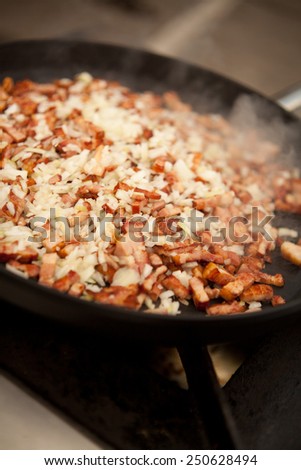Bacon and onion cut into pieces frying on a frying pan. Home-made meal. Food, restaurant, macro perspective, nobody.