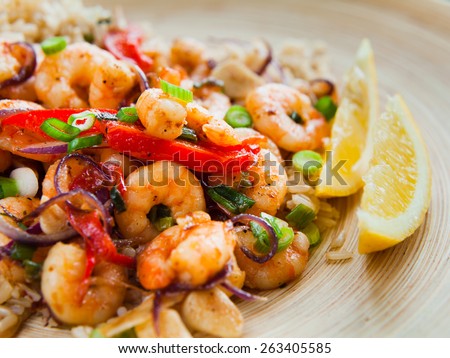 Fried king prawns with brown rice and vegetables: red pepper and onions. Served on a wooden plated with cut chives, spring onions and two pieces of lemon.Macro perspective, nobody, restaurant, menu.