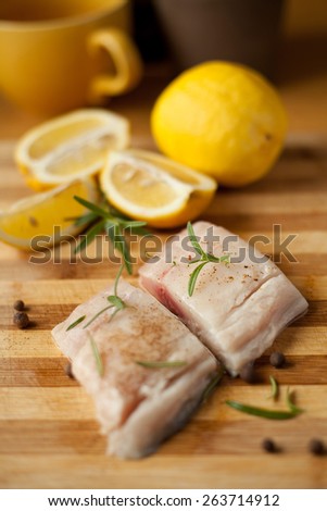 Pieces of fresh fish. Fish and lemon on a wooden desk with rosemary twig. Macro, fresh food, natural ingredients. Helpful on a diet. Healthy food. White fish fillets