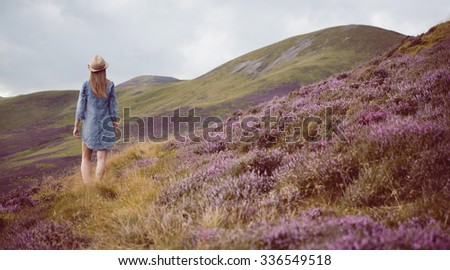 young beautiful woman  in blue dress  the heather meadows in Scotland watching the mountains.