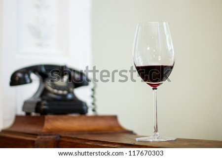 Glass of wine over a wooden table and an old clock on the background.