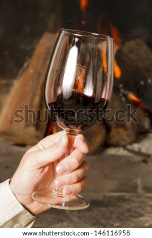 Hand holding cup of Wine by the fireplace, glasses of wine.