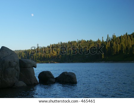 The moon rising over Icehouse reservoir in the Sierra with granite rocks in the foreground
