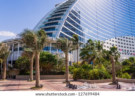 DUBAI, UAE - FEBRUARY 03: Palm trees waving in the wind and giant chess board in front of Jumeirah Beach Hotel, wave-shaped luxury resort, well-known Dubai landmark, on February 3, 2013, Dubai, UAE.