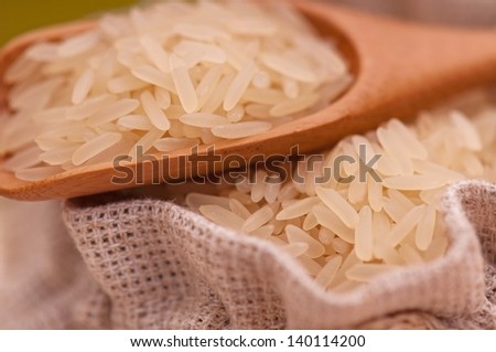 Uncooked rice in bamboo spoon on a burlap bag close-up