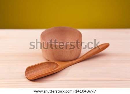 Empty wooden bowl with bamboo spoon on a wooden surface over dark yellow background