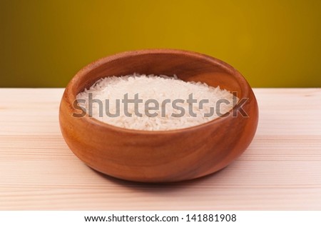 White rice in the bamboo bowl on a wooden surface over dark yellow background