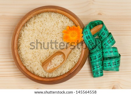 Raw rice in a bamboo bowl with tape measure over wooden surface