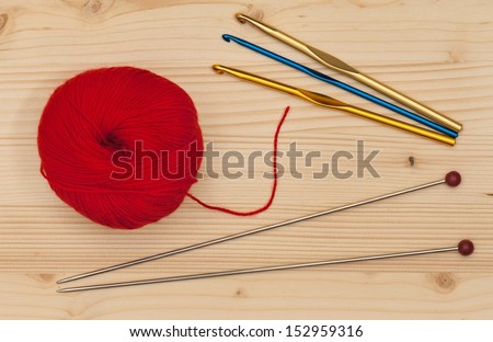 Knitting  hook and spokes with woolen threads over wooden surface