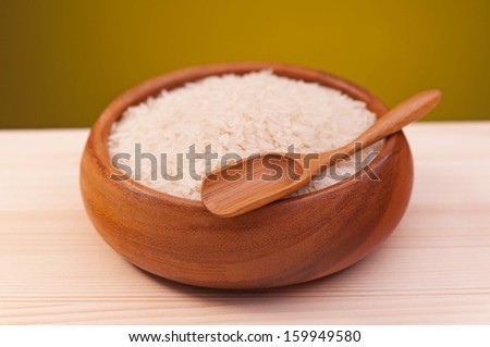 Raw rice in the bamboo bowl on wooden surface over dark yellow background