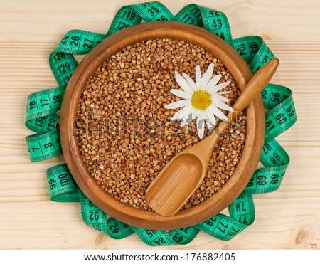 Raw buckwheat in a bamboo bowl with tape measure on a wooden surface