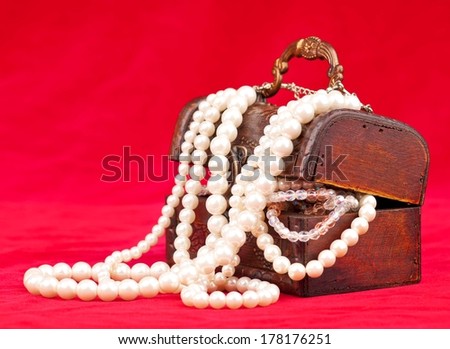 Jewel box with pearl necklace over red background
