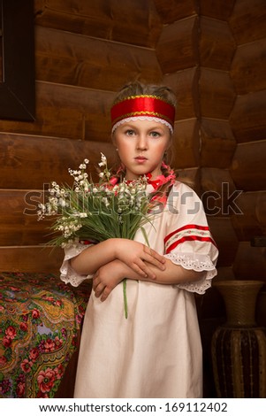 Girl in Russian national sundress. Folk dress.Cute little blonde girl in the hut. Holding a bouquet of flowers and lily of the valley