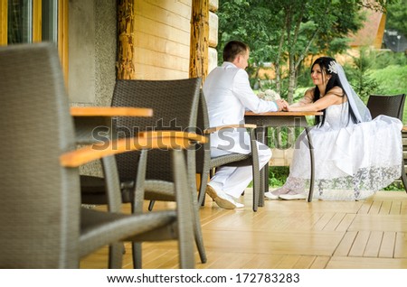 Happy bride and groom sit at a table and holding hands