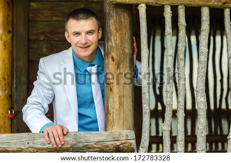 Portrait of the groom on the wooden porch near the wooden lattice