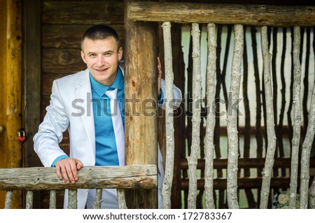 Portrait of the groom on the wooden porch near the wooden lattice