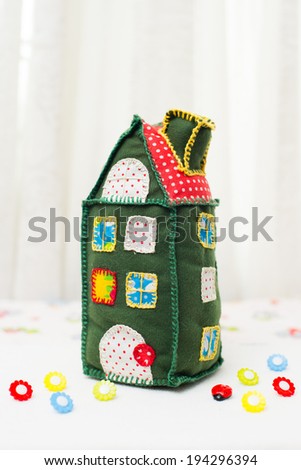 Handmade soft toy Green House  with bright colored windows on a background of flower fields buttons