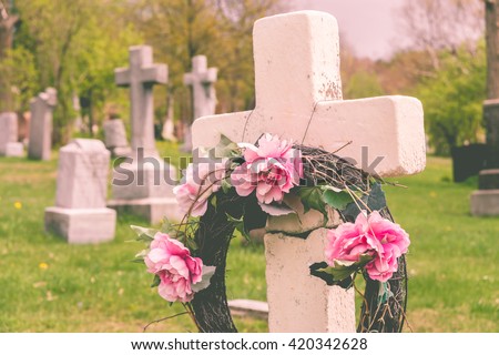 Funeral wreath with pink flower on a cross, in a cemetery, with a vintage filter.