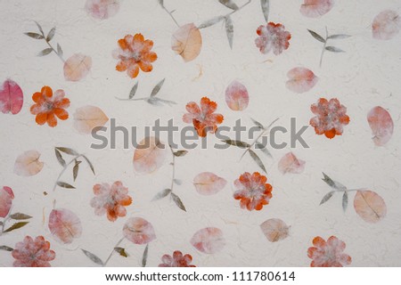 Sheet of handmade rice paper showing the natural elements used to make the paper including red flowers and green leaves.