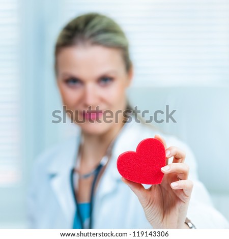 Pretty Young Female Doctor Is Showing a Red Heart in Ambulance (shallow depth of field, color toned image)