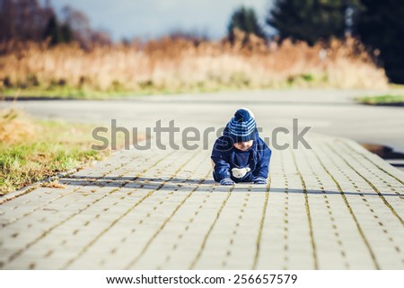Little toddler boy is crawling on a sidewalk on outdoor walk in a neighborhood
