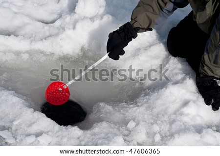A gloved hand scooping out ice from a hole for ice fishing