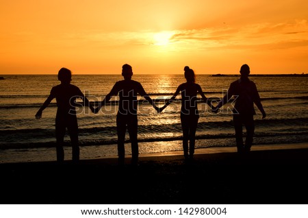Group of happy people parting on the beach at sunrise, all holding hands