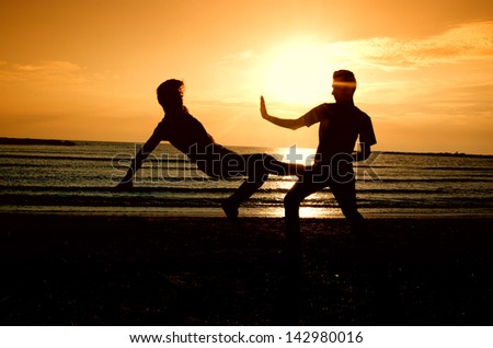 Group of happy people parting on the beach at sunrise, people fighting, doing karate