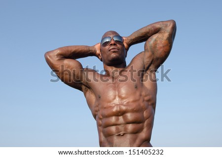 Black bodybuilder wearing sunglasses and showing off his big muscles. Black bodybuilder topless. Strong man with perfect abs, shoulders,biceps, triceps and chest. Isolated on white background