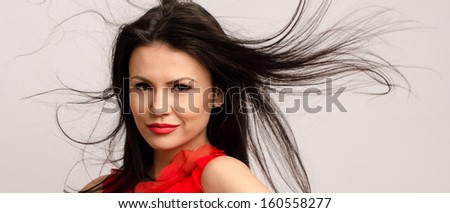 Beautiful brunette girl with long hair. Young attractive woman with red lips wearing a red blouse with hair in the air