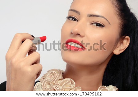 Portrait of a beautiful brunette woman applying red lipstick on her lips. Woman with red lips  holding with her hand with black fingernails a red lipstick