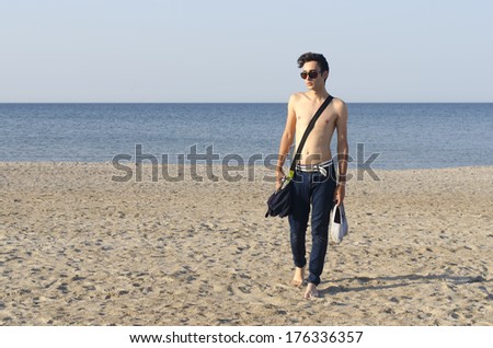 Young man enjoying his time on the beach, young man walking on the sand and having a tan