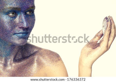 Beautiful face of a woman covered in glitter Close up of a woman\'s face covered in blue and purple glitter using a beauty mirror