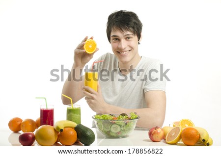 Happy man making orange juice. Cheerful young man eating healthy salad,fruits,orange juice and green smoothie.