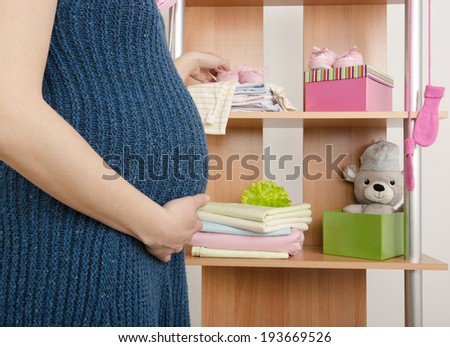 Pregnant woman shopping for clothes for her newborn baby. Dressing closet with clothes arranged on hangers.Colorful wardrobe of newborn,kids, babies full of all clothes, shoes,accessories and toys