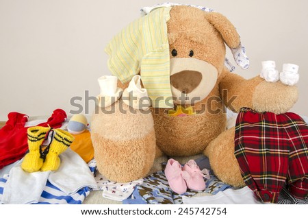 Bear toy on a bed with different colorful new born clothes.Colorful wardrobe of newborn,kids, babies full of all clothes, shoes,accessories and toys