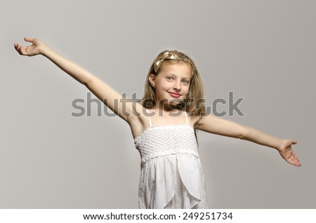 Beautiful young blonde girl in white dress smiling and playing. Kid enjoying life and having fun
